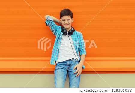 Portrait of happy modern teenage boy listening to music with headphones on orange wall background 119395058