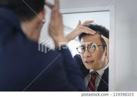 A businessman in his late 30s who is concerned about his hairline while looking in the mirror 119398323