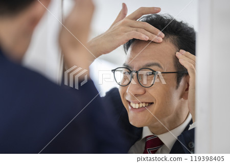 A smiling businessman in his late teens checking his hairline in the mirror A smiling businessman in his late teens checking his hairline in the mirror 119398405