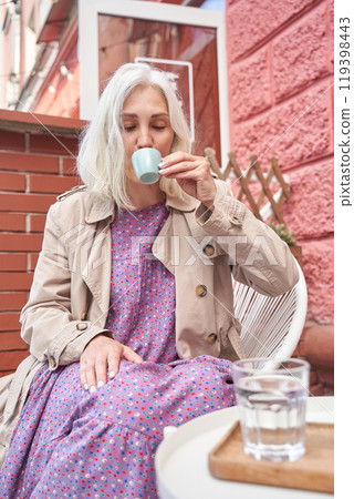 Elderly woman enjoying coffee outdoors in cozy urban setting on a relaxing day 119398443