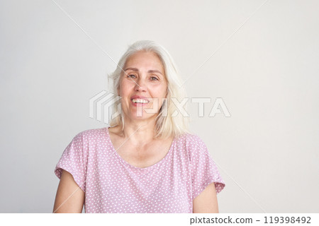 Confident senior woman with white hair in casual polka dot shirt smiling against 119398492