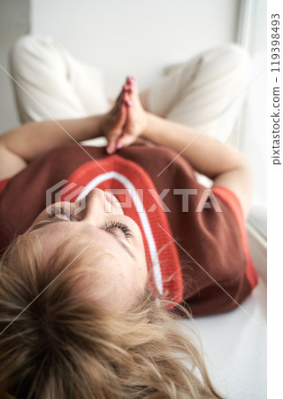 Relaxed woman meditating indoors with closed eyes and hands in prayer pose 119398493