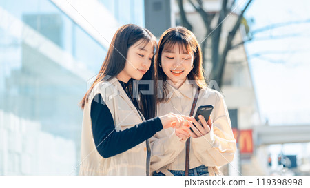 Young women with friends looking at a smartphone in the city 119398998