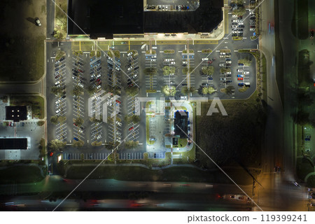 View from above of many parked cars on illuminaded parking lot with lines and markings for parking places and directions. Place for vehicles in front of a shopping mall center 119399241