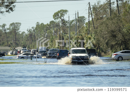 Flooded american street with moving vehicles surrounded with water in Florida residential area. Consequences of hurricane natural disaster 119399571