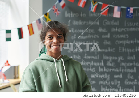 Portrait of Black female student smiling at camera while standing by blackboard in classroom, copy space Portrait of Black female student smiling at camera while standing by blackboard in classroom, copy space 119400230