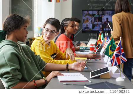 Multiethnic group of students sitting at table with country flags and communicating during international conference, copy space Multiethnic group of students sitting at table with country flags and communicating during international conference, copy space 119400251