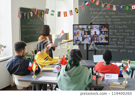 Back view at group of students looking at computer screen with video chat during international online conference in school classroom Back view at group of students looking at computer screen with video chat during international online conference in school classroom 119400260