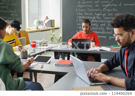 African American young woman using laptop in school classroom with group of students in foreground, copy space 119400269