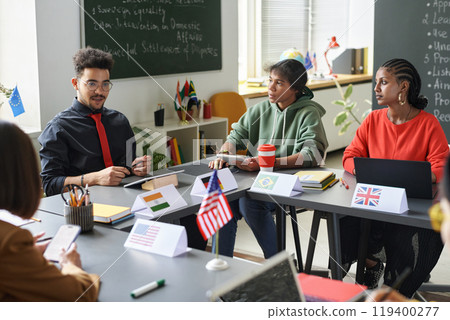 Group of students sitting at seminar together with teacher speaking in foreground during lesson in school classroom 119400277