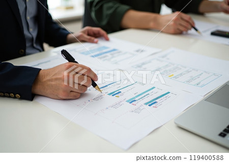 Hands of two individuals engaged in reviewing project documents at workplace, focusing on details and notes for strategic planning and analysis 119400588