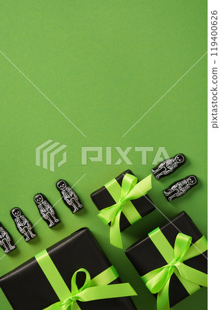 Halloween gift boxes with green ribbons and skeleton decorations on green background. Place for your text. 119400626
