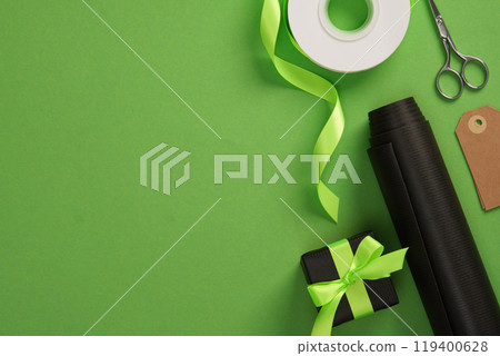 Black and green gift wrap banner with black wrapping paper, scissors, tags and ribbon on green background. Space for your text. 119400628