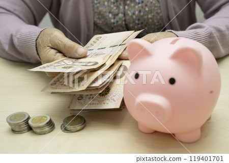 Retired elderly woman counting coins money with piggy bank and worry about monthly expenses and treatment fee payment. Retired elderly woman counting coins money with piggy bank and worry about monthly expenses and treatment fee payment. 119401701