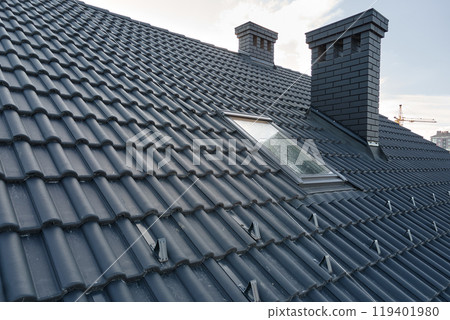Closeup snow guard for safety in winter on house roof top covered with ceramic shingles. Tiled covering of building 119401980