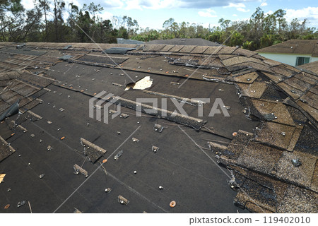 Damaged house roof with missing shingles after hurricane Ian in Florida. Consequences of natural disaster Damaged house roof with missing shingles after hurricane Ian in Florida. Consequences of natural disaster 119402010