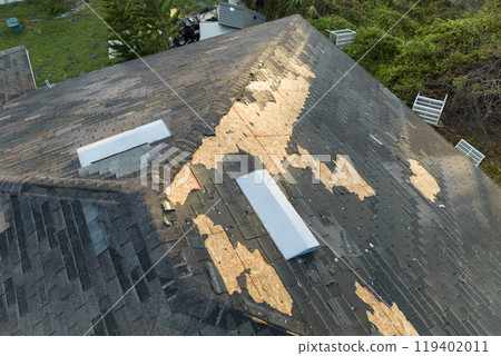 Damaged house roof with missing shingles after hurricane Ian in Florida. Consequences of natural disaster 119402011