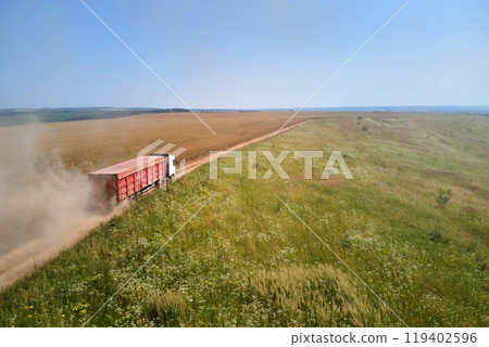 Aerial view of lorry cargo truck driving on dirt road between agricultural wheat fields. Transportation of grain after being harvested by combine harvester during harvesting season 119402596