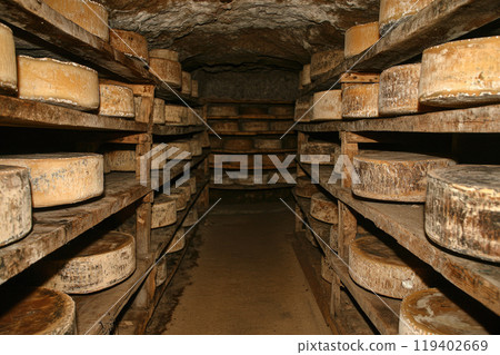Cheese factory warehouse with shelves stacked with rows of Whole wheel cheese Cheese factory warehouse with shelves stacked with rows of Whole wheel cheese 119402669