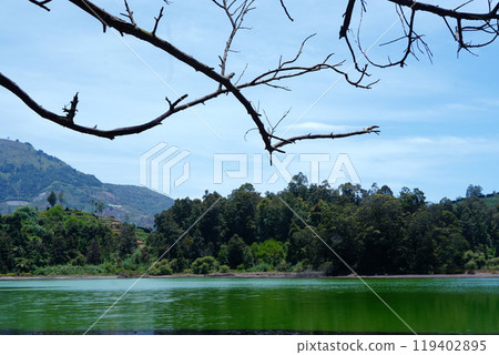 Serene Dieng landscape with a lake, mountains, and a tree branch against a blue sky. Serene Dieng landscape with a lake, mountains, and a tree branch against a blue sky. 119402895
