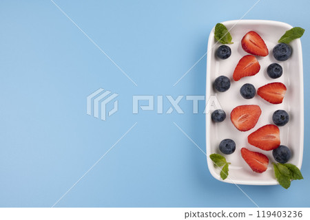 Plate with berries and mint leaves on a blue background, template for inserting text, menu. High quality photo Plate with berries and mint leaves on a blue background, template for inserting text, menu. High quality photo 119403236