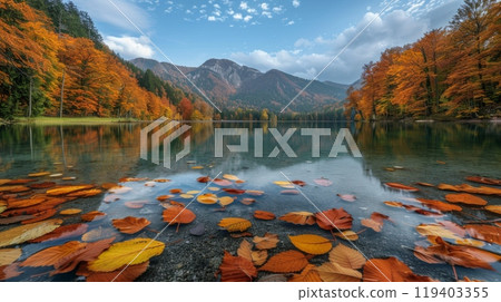 Autumn leaves float on the surface of the lake against the backdrop of forest and mountains. 119403355