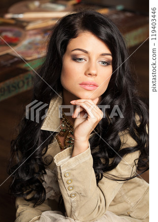 Pretty brunette woman posing in art studio. Young lady with long curly hair and make-up  119403446