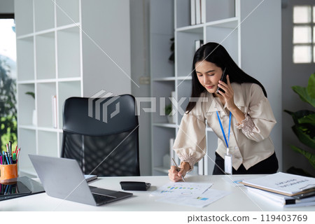 Focused Businessman Analyzing Documents at Modern Office Desk with Laptop and Smartphone for Professional Work and Productivity 119403769