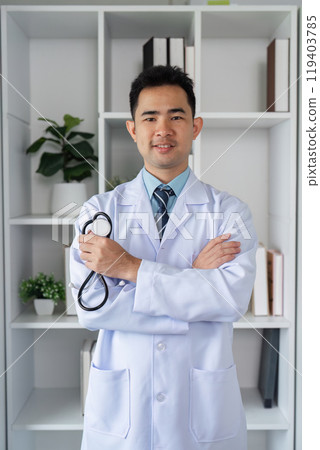Confident Male Doctor in White Coat with Stethoscope Standing in Modern Medical Office Environment 119403785