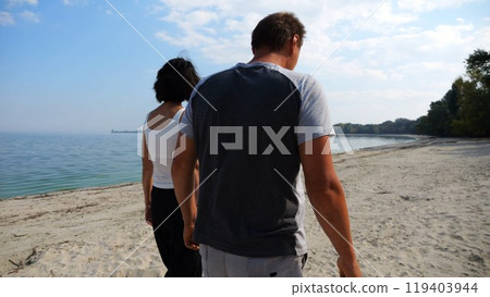 Couple holding hands of each other and walking at coast. Happy pair going along seashore at sunny day. Lovers spending time together at resort. Concept of vacation or holiday. Slow mo Couple holding hands of each other and walking at coast. Happy pair going along seashore at sunny day. Lovers spending time together at resort. Concept of vacation or holiday. Slow mo 119403944