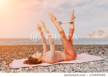 Woman sea pilates. Sporty happy middle aged woman practicing fitness on beach near sea, smiling active female training with ring on yoga mat outside, enjoying healthy lifestyle, harmony and meditation 119404466