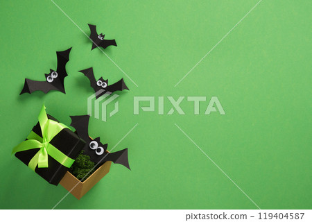 Banner with Halloween Gift Box with green neon ribbon with paper bats flying out of it. Space for your text, advert, invitation. 119404587