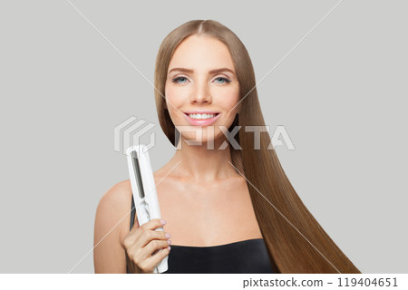 Portrait of smiling woman with long straight healthy hairstyle using straightening iron Portrait of smiling woman with long straight healthy hairstyle using straightening iron 119404651