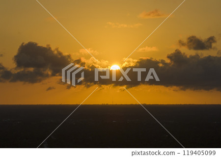 Bright sunset over dark rural land. Setting sun behind vivid orange and yellow clouds Bright sunset over dark rural land. Setting sun behind vivid orange and yellow clouds 119405099