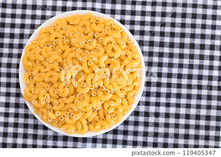 Uncooked Chifferi Rigati Pasta in White Cup on Black Checkered Towel 119405347