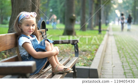 Small happy child girl sitting on a bench resting in summer park. Small happy child girl sitting on a bench resting in summer park. 119405430