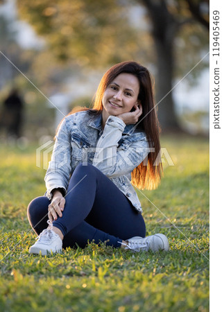 Happy young woman resting outside on green grassy meadow in city park 119405469