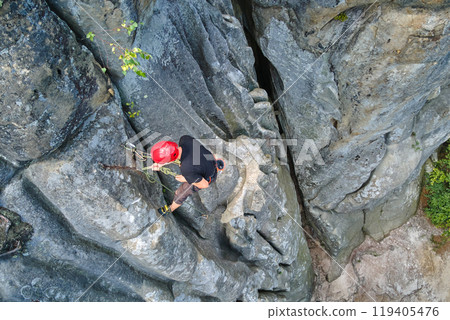 Determined climber clambering up steep wall of rocky mountain. Sportsman overcoming difficult route. Engaging in extreme sports and rock climbing hobby concept. 119405476