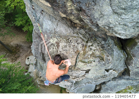 Determined climber clambering up steep wall of rocky mountain. Sportsman overcoming difficult route. Engaging in extreme sports and rock climbing hobby concept. 119405477
