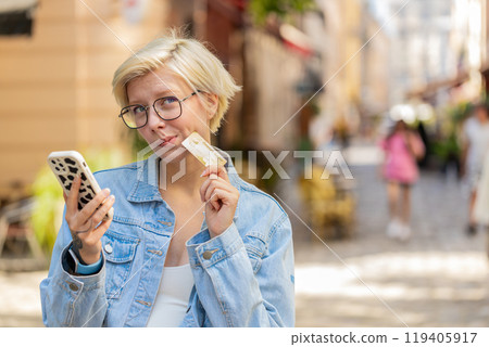 Happy Caucasian woman using credit card smartphone while purchases online shopping on city street 119405917