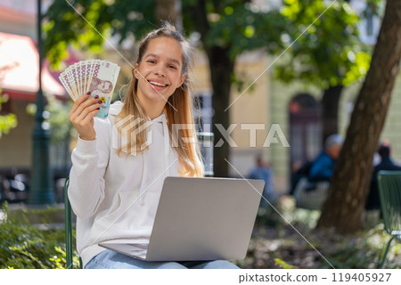 Happy rich woman using laptop winner victory holding cash money in Ukrainian hryvnias UAH banknotes Happy rich woman using laptop winner victory holding cash money in Ukrainian hryvnias UAH banknotes 119405927