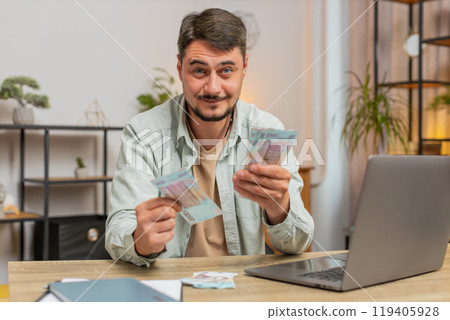 Rich happy Caucasian man counting money cash using laptop calculate domestic bills at home table Rich happy Caucasian man counting money cash using laptop calculate domestic bills at home table 119405928
