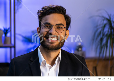 Portrait of happy smiling bearded Indian business man at home office looking at camera Portrait of happy smiling bearded Indian business man at home office looking at camera 119405965