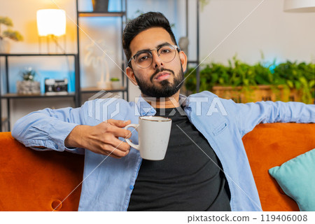 Tired smiling Indian man drinking cup of warm coffee or herbal tea in the morning relaxing enjoying 119406008