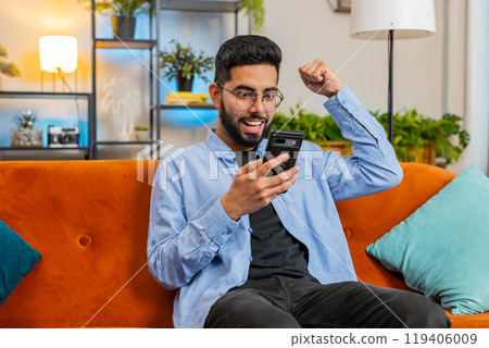 Surprised excited Indian man use smartphone reading good news amazed by online bet bid game win Surprised excited Indian man use smartphone reading good news amazed by online bet bid game win 119406009