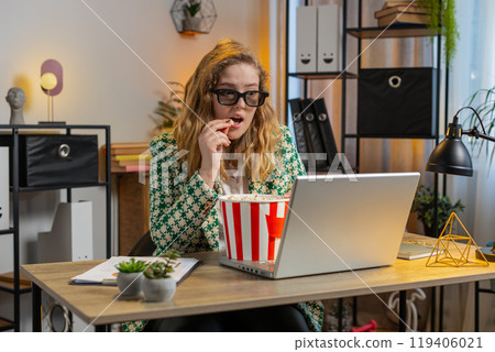 Businesswoman taking break from work wearing 3D glasses eating popcorn and watching movie at office 119406021