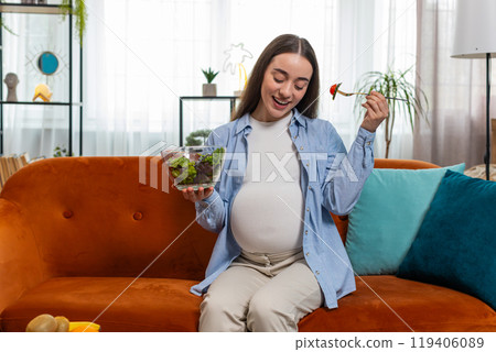 Happy pregnant woman with great appetite eats vegetable salad sitting on sofa healthy food self-care Happy pregnant woman with great appetite eats vegetable salad sitting on sofa healthy food self-care 119406089