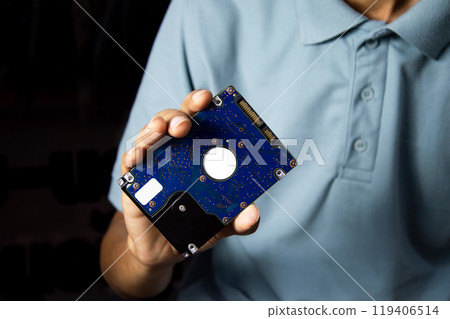 A male technician holds a 2.5-inch hard drive, a data storage device. A male technician holds a 2.5-inch hard drive, a data storage device. 119406514