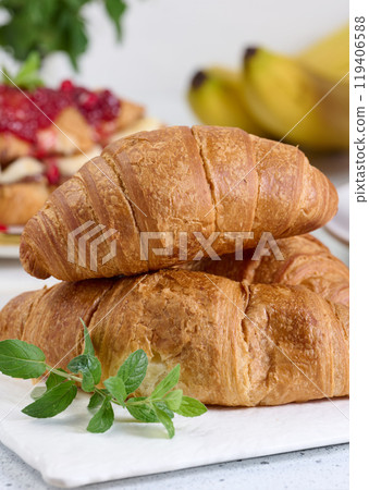 Baked croissants and a sprig of mint on a white table, breakfast Baked croissants and a sprig of mint on a white table, breakfast 119406588