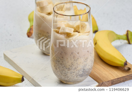 Glass with chia and yogurt dessert garnished with fresh banana slices on white table Glass with chia and yogurt dessert garnished with fresh banana slices on white table 119406629